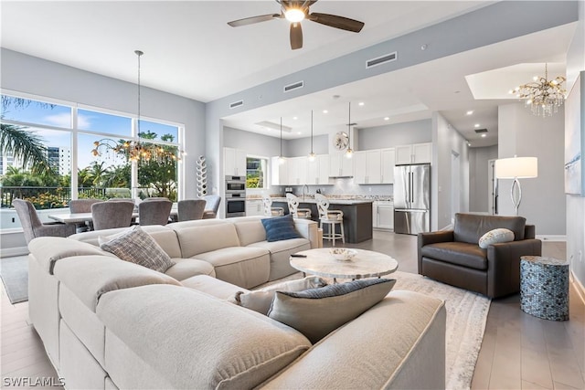 living room featuring ceiling fan with notable chandelier, light wood-type flooring, and sink