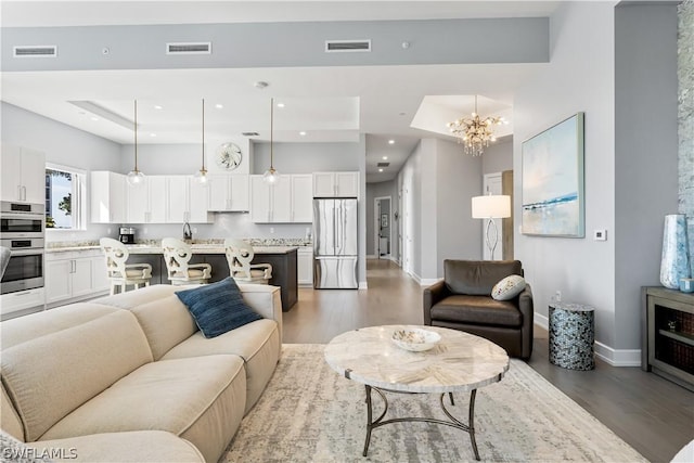 living room featuring dark hardwood / wood-style floors, a raised ceiling, and a notable chandelier