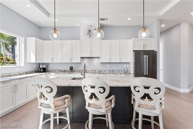 kitchen featuring high end refrigerator, decorative light fixtures, and a kitchen island with sink