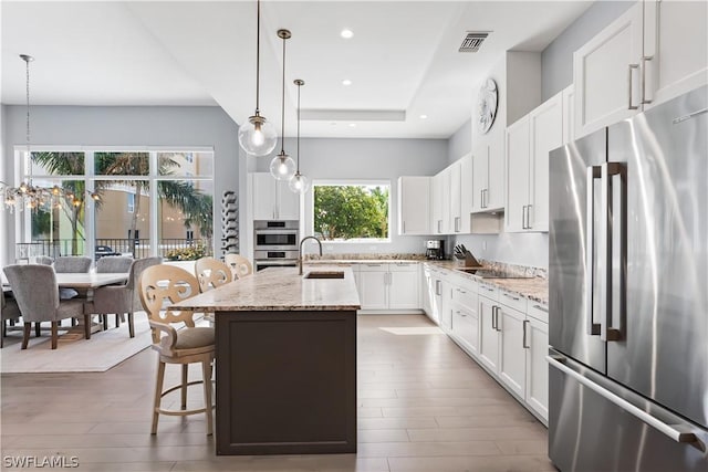 4142 Bay Beach Ln Unit 206, Fort Myers Beach, FL 33931 - kitchen with appliances with stainless steel finishes, wood finished floors, light stone counters, a kitchen island with sink, and white cabinetry