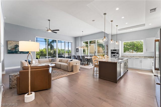 kitchen with light stone countertops, ceiling fan, hanging light fixtures, a kitchen island with sink, and white cabinets