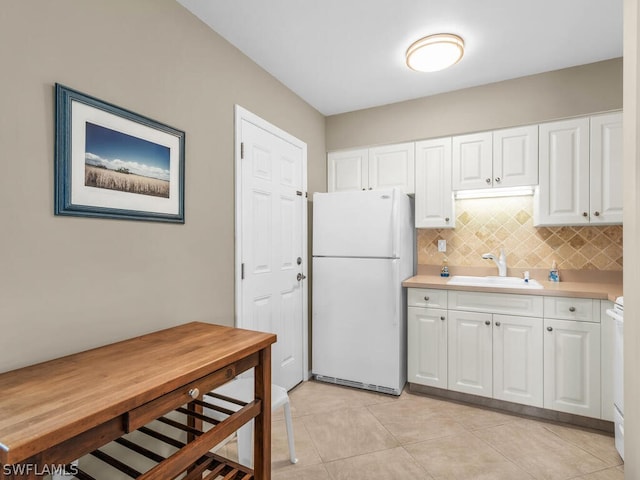 kitchen with tasteful backsplash, sink, white fridge, white cabinetry, and light tile patterned flooring