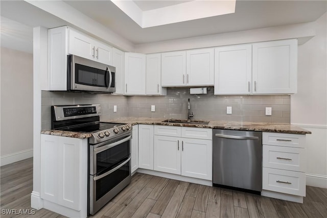 kitchen with sink, appliances with stainless steel finishes, dark stone counters, and white cabinetry