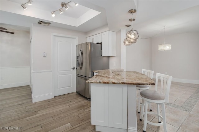 kitchen featuring light hardwood / wood-style flooring, hanging light fixtures, light stone countertops, white cabinetry, and stainless steel fridge with ice dispenser