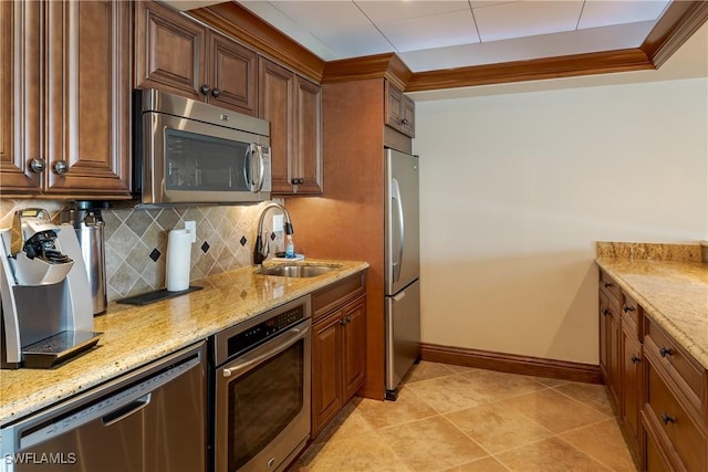 kitchen with tasteful backsplash, stainless steel appliances, light stone countertops, crown molding, and sink