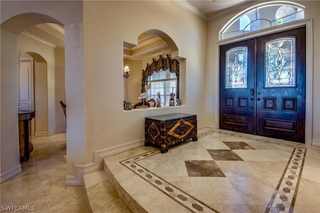 foyer entrance featuring arched walkways, crown molding, and baseboards