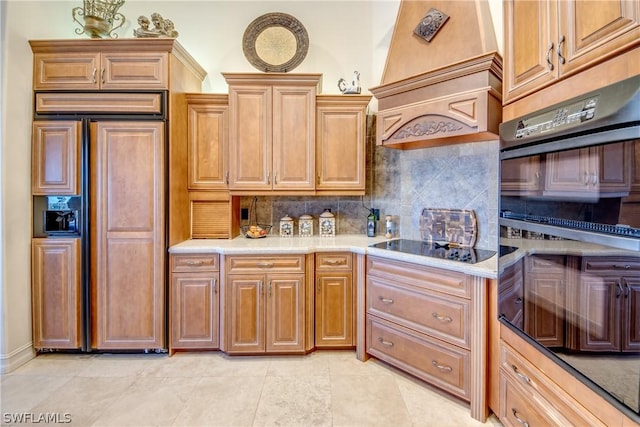 kitchen with black electric stovetop, light countertops, custom range hood, decorative backsplash, and paneled built in refrigerator