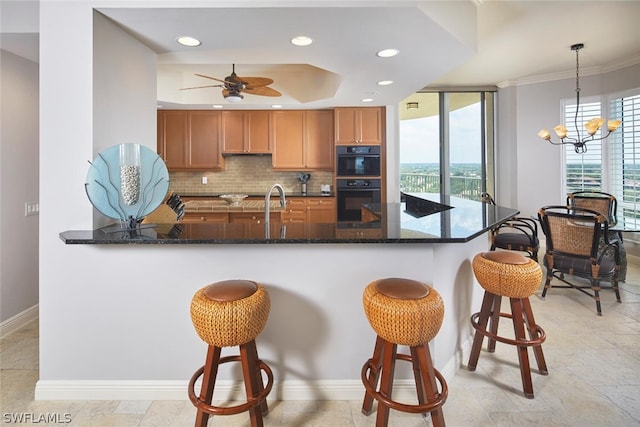 kitchen featuring double oven, dark stone countertops, kitchen peninsula, pendant lighting, and ornamental molding