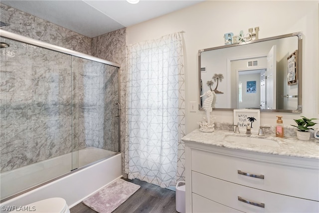 full bathroom with shower / bath combination with glass door, hardwood / wood-style flooring, vanity, and toilet