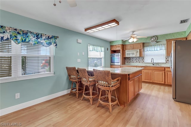 kitchen with light hardwood / wood-style flooring, stainless steel appliances, ceiling fan, a breakfast bar area, and sink