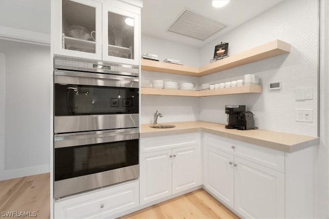 kitchen with white cabinets, light hardwood / wood-style flooring, double oven, and sink