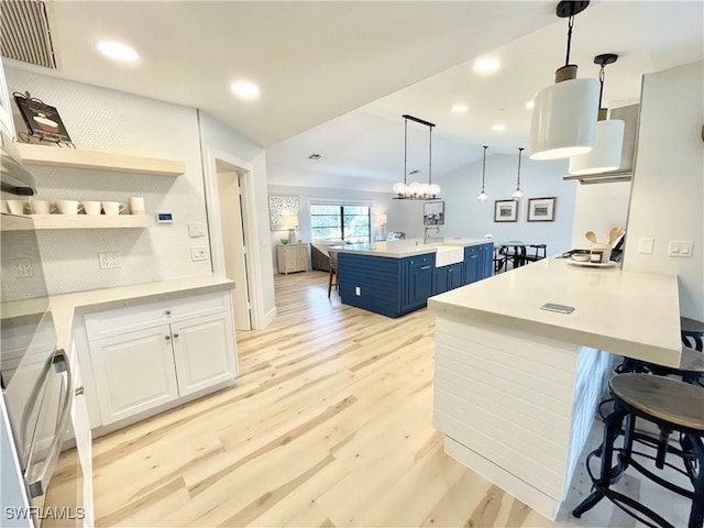 kitchen featuring blue cabinetry, white cabinetry, a kitchen breakfast bar, vaulted ceiling, and light wood-type flooring