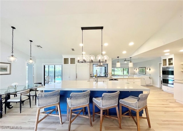 kitchen featuring pendant lighting, lofted ceiling, white cabinets, light wood-type flooring, and a breakfast bar area