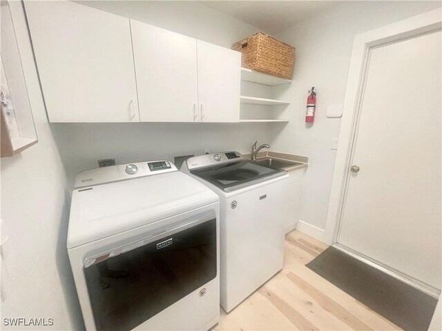 laundry area with washer and dryer, light wood-type flooring, cabinets, and sink