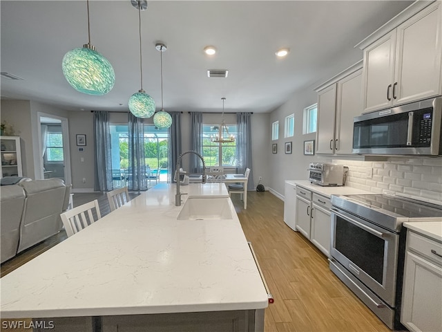 kitchen with appliances with stainless steel finishes, decorative light fixtures, a kitchen island with sink, and sink