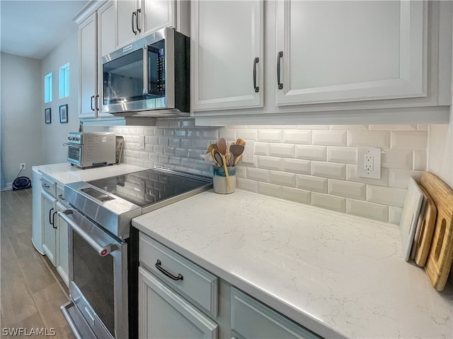 kitchen featuring light stone counters, appliances with stainless steel finishes, wood-type flooring, and backsplash