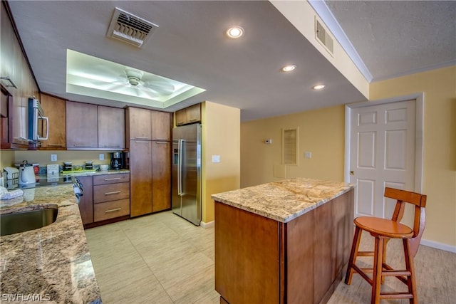 kitchen with a breakfast bar, appliances with stainless steel finishes, light stone counters, and a raised ceiling