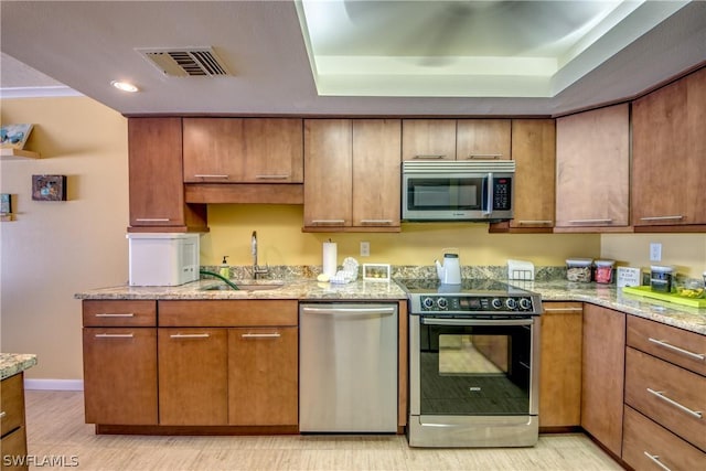 kitchen with appliances with stainless steel finishes, light stone counters, and sink