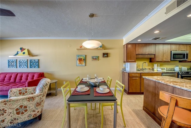 kitchen with sink, light stone counters, pendant lighting, a textured ceiling, and ornamental molding