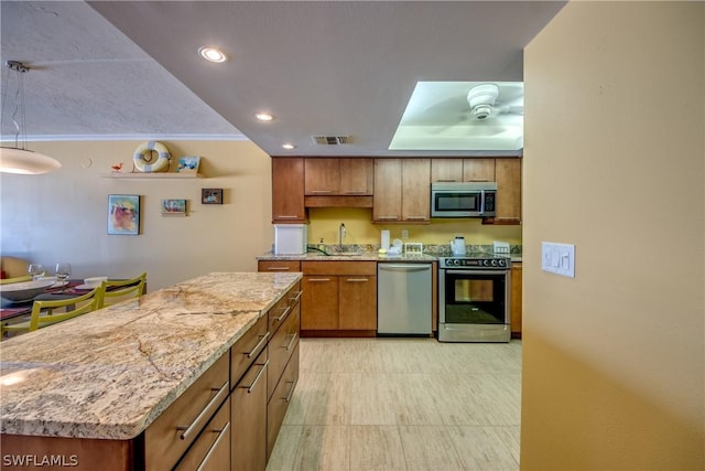 kitchen with light stone counters, stainless steel appliances, a tray ceiling, sink, and a center island