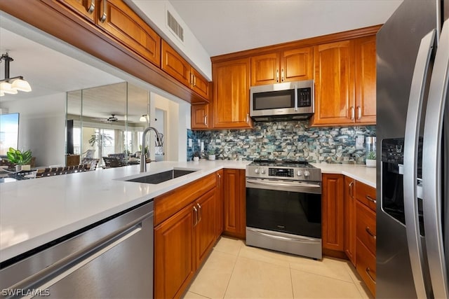 kitchen with appliances with stainless steel finishes, backsplash, sink, light tile patterned floors, and decorative light fixtures