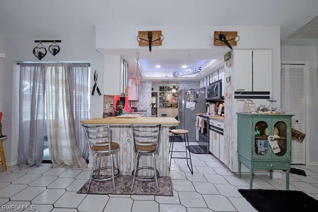 kitchen featuring stainless steel appliances, white cabinets, light tile floors, and a raised ceiling