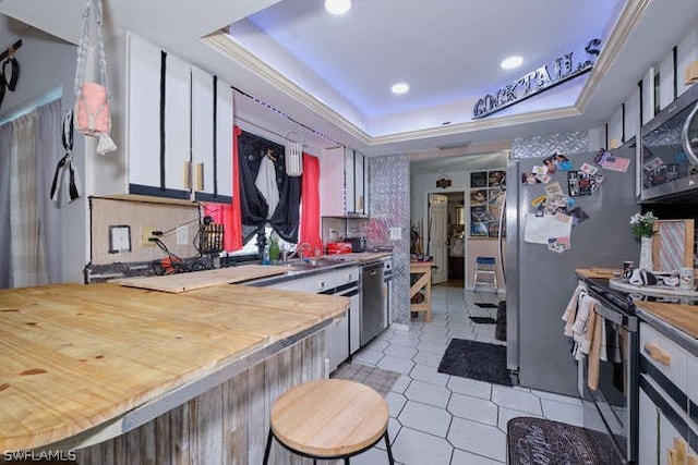 kitchen featuring stainless steel appliances, light tile flooring, a tray ceiling, white cabinets, and sink