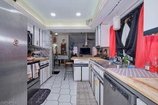 kitchen with appliances with stainless steel finishes, sink, light tile flooring, white cabinetry, and a raised ceiling