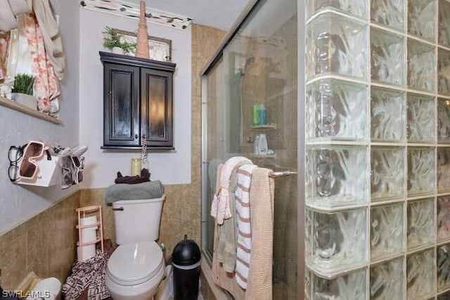 bathroom with tile walls, toilet, and a shower with shower door