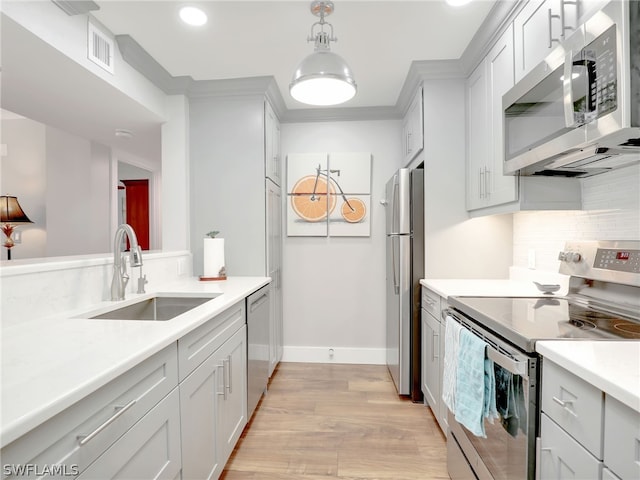 kitchen featuring tasteful backsplash, stainless steel appliances, light hardwood / wood-style floors, decorative light fixtures, and sink