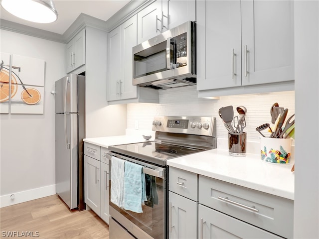 kitchen with ornamental molding, appliances with stainless steel finishes, light wood-type flooring, and tasteful backsplash