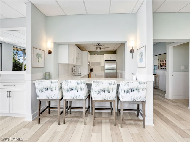 kitchen with stainless steel fridge, a breakfast bar, kitchen peninsula, white cabinetry, and light hardwood / wood-style flooring