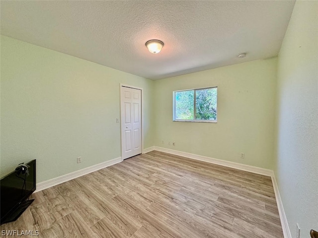 spare room with a textured ceiling and light hardwood / wood-style floors