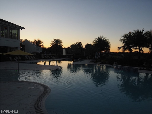 pool at dusk with a patio area and pool water feature