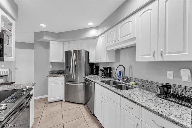 kitchen with light stone counters, appliances with stainless steel finishes, light tile floors, sink, and white cabinetry