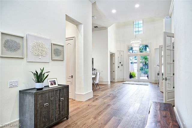 foyer with light hardwood / wood-style floors, french doors, an inviting chandelier, and a high ceiling