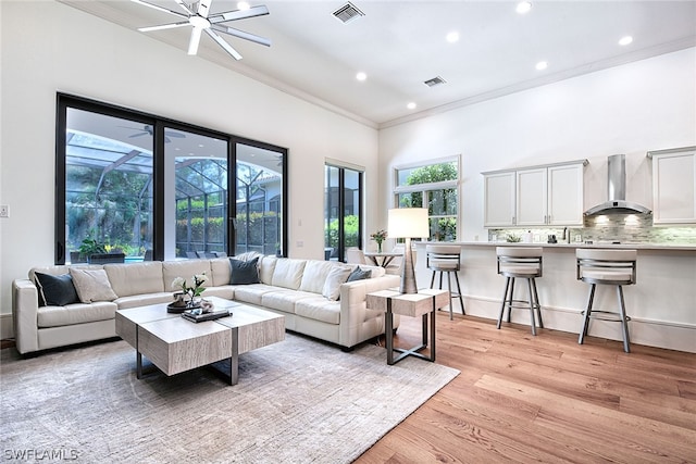 living room with crown molding, ceiling fan, and light wood-type flooring