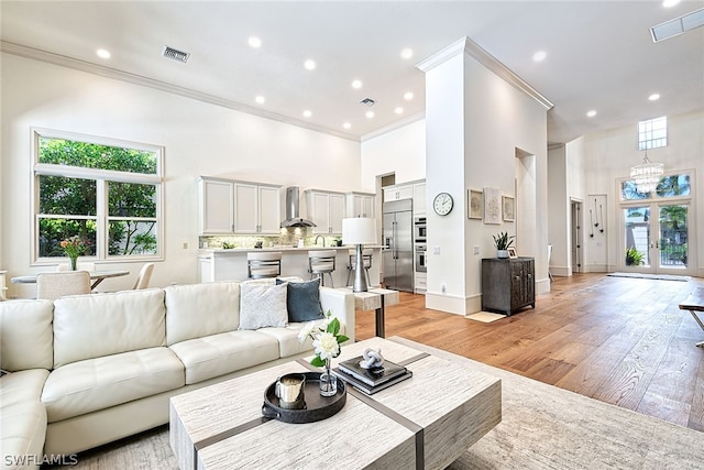 living room featuring ornamental molding, light hardwood / wood-style floors, and a towering ceiling