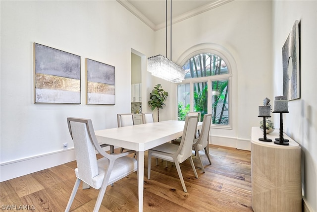 dining area with ornamental molding, a notable chandelier, a towering ceiling, and light wood-type flooring