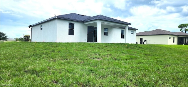 rear view of property featuring a lawn and stucco siding