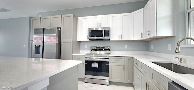 kitchen with white cabinets, appliances with stainless steel finishes, light stone counters, marble finish floor, and a sink