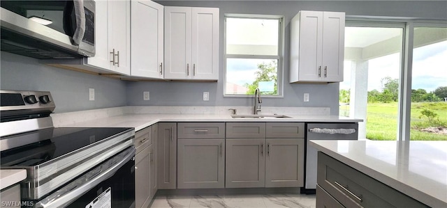 kitchen featuring appliances with stainless steel finishes, light stone countertops, marble finish floor, gray cabinetry, and a sink