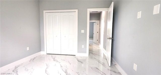 unfurnished bedroom featuring a closet, marble finish floor, and baseboards