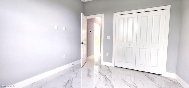 unfurnished bedroom featuring a closet, marble finish floor, and baseboards