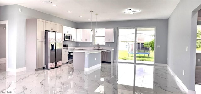 kitchen featuring baseboards, a kitchen island, appliances with stainless steel finishes, light countertops, and a sink