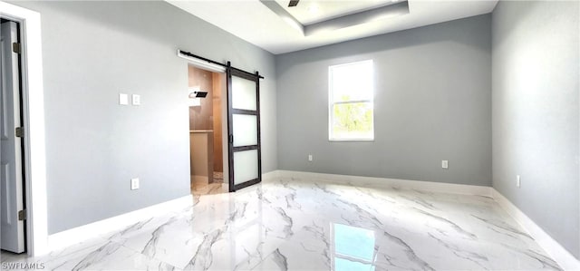 spare room featuring a raised ceiling, marble finish floor, baseboards, and a barn door