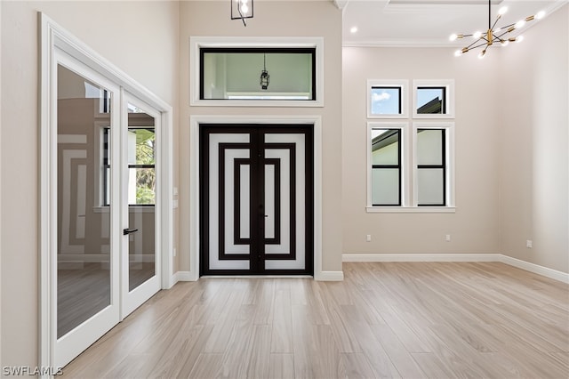 entrance foyer with ornamental molding, french doors, light wood-type flooring, and a chandelier