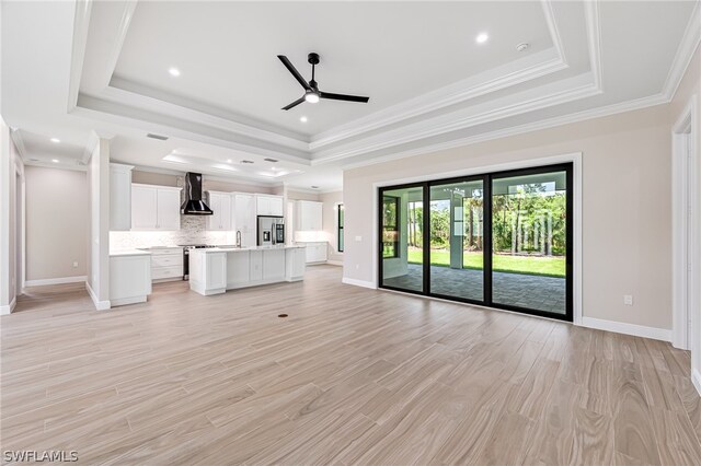 unfurnished living room featuring light hardwood / wood-style floors, ornamental molding, ceiling fan, and a raised ceiling