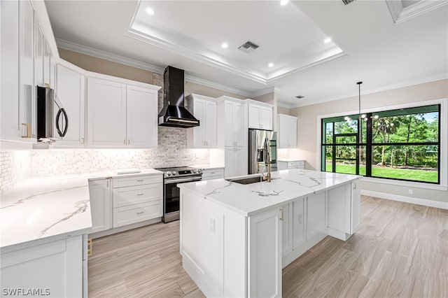 kitchen with stainless steel appliances, an island with sink, wall chimney exhaust hood, tasteful backsplash, and a raised ceiling