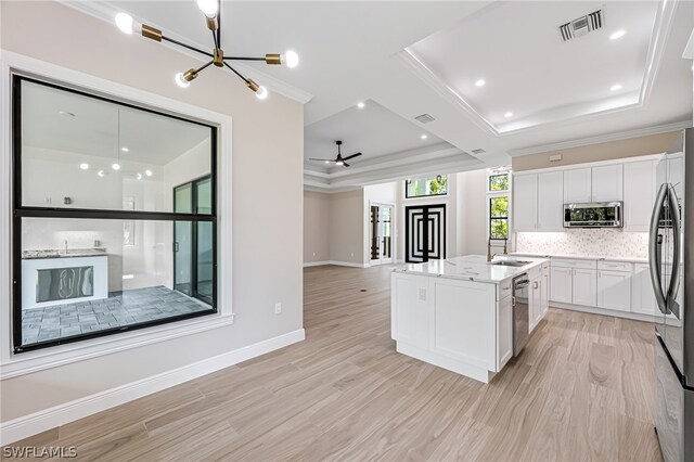 kitchen with stainless steel appliances, white cabinets, light hardwood / wood-style floors, and a raised ceiling